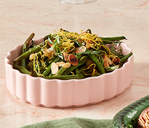 A bowel of air-fried green beans. The beans have been topped with flaked almonds, herbs and lemon zest.