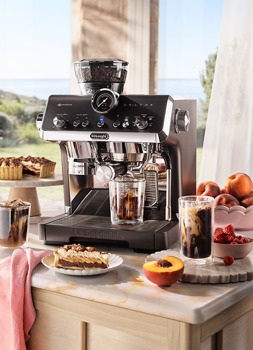 The De'Longhi La Specialista Opera Manual Coffee Machine on a outdoor kitchen bench. Around it are deserts, glasses of iced coffee and a bowl of raspberries.