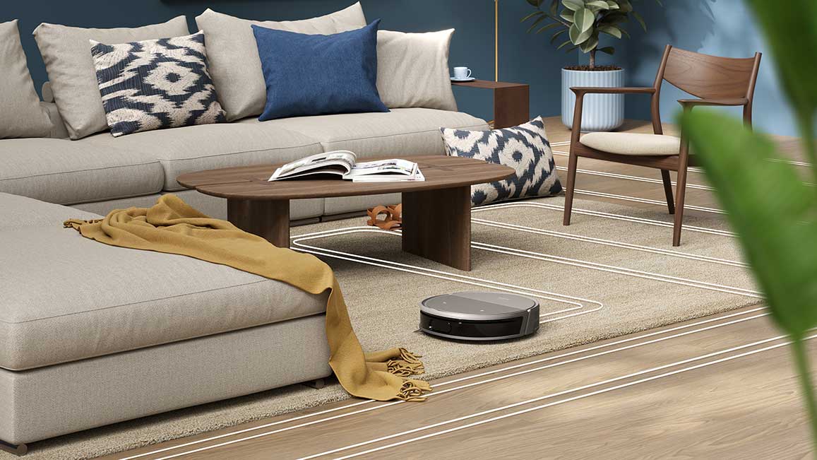 Photo of a robotic vacuum cleaner at work in a living room, finding its way around obstacles including a lounge chair, coffee table, armchair, and a decorative throw that is dangling from the couch.
