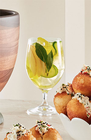 A glass of a Sangria Bianco cocktail garnished with sliced peaches and cucumbers.