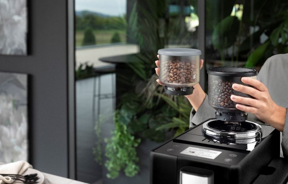 Person holding two De'Longhi Rivelia bean canisters.