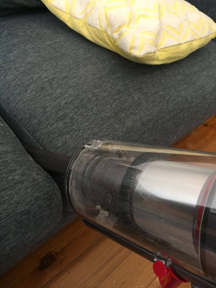 A Dyson V11 Absolute Extra Cordless Vacuum cleaning sofa with the crevice tool attached.