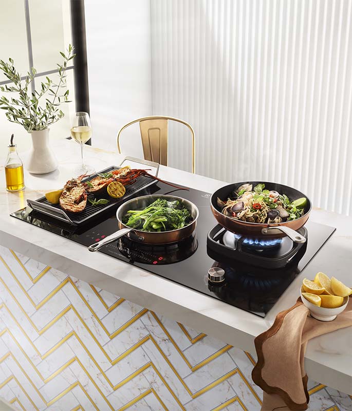 The Electrolux 900mm UltimateTaste Cooktop with Lobster, Greens and Noodles cooking on top.