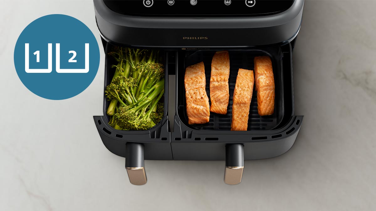 Photo showing the Philips 3000 Series with its dual baskets open, with broccolini in the smaller left drawer and four salmon steaks in the larger right drawer.