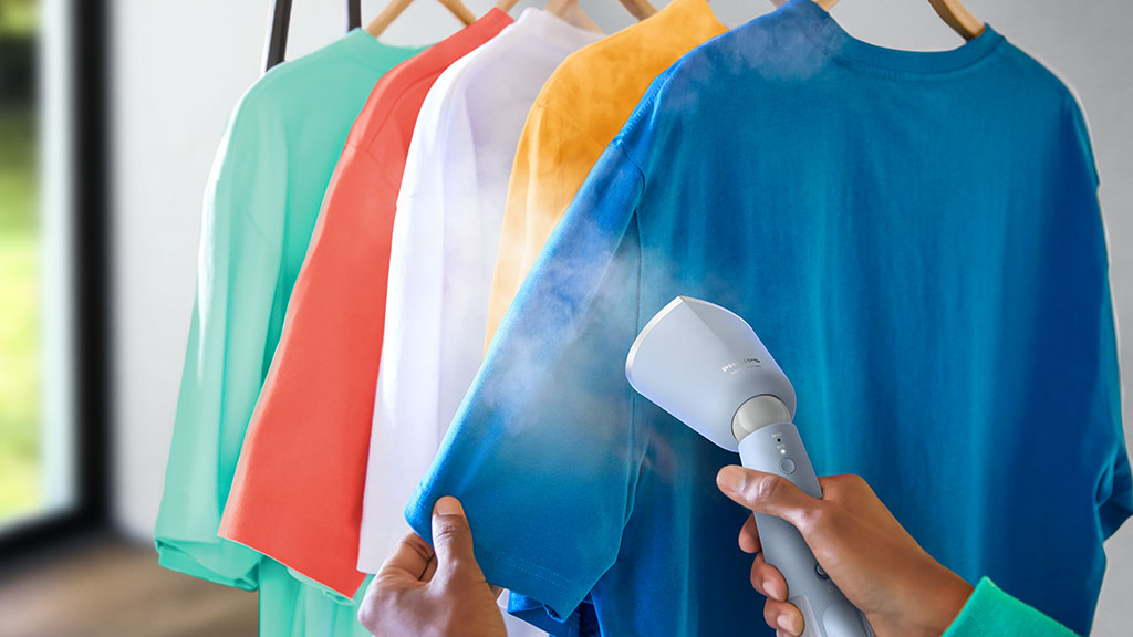 A garment steamer being used on a blue t-shirt hung up on a clothes hanger.