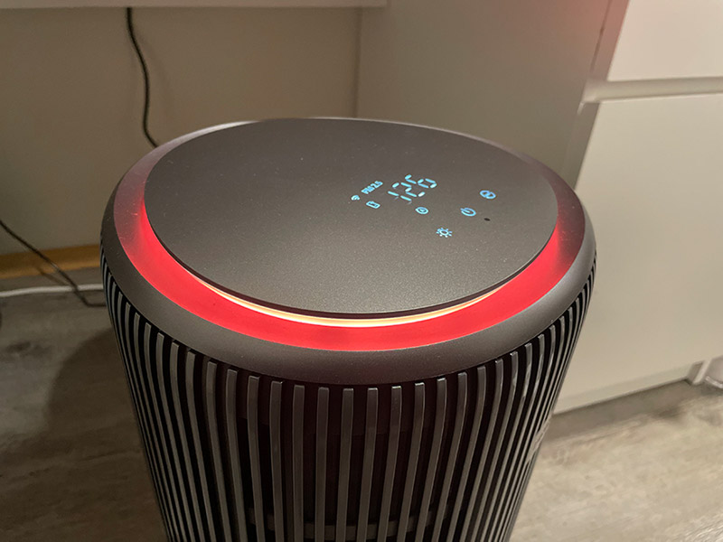 An air purifier mounted on the floor of a room with a bright red ambient light ring indicating a poor air quality reading.