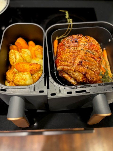 Photo showing a delicious meal cooked in the dual baskets of the Philips 3000 Series Air Fryer, with roasted potatoes in the left basket and a pork roast in the right basket.