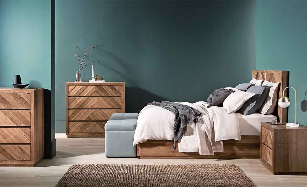 Natural timber bedroom furniture set against a slate green bedroom wall.