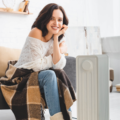 Woman sitting beside an oil column heater wrapped in a checkered blanket